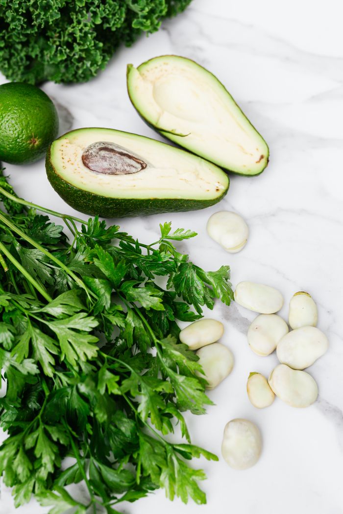 hero-img-02 Crisp parsley, ripe avocado, broad beans, and lime on a white marble surface, a fresh culinary display.