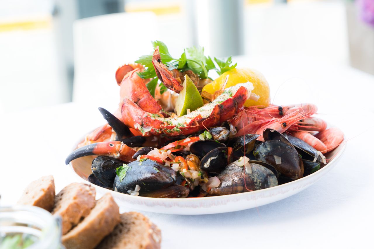 gallery-4 A vibrant seafood platter featuring lobster, shrimp, mussels, and lemon on a white plate.