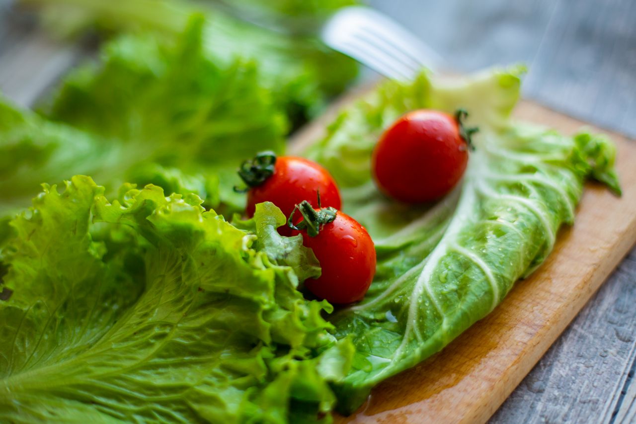 High angle of fresh red tomatoes on green lettuce leaves placed on wooden cutting board in daylight